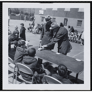 Two judges inspecting a cat on the table while other participants look on during a Boys' Club Pet Show