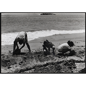 Three children play in the sand at the shoreline on a beach