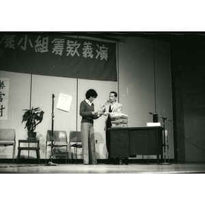 Man and woman discuss the contents of a piece of paper during a skit on stage at the Chinatown Task Force Fundraiser