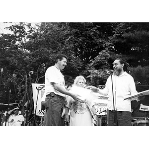 Two men and one woman standing on the outdoor stage at Festival Betances holding pieces of paper or certificates.