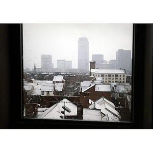 View out a window of the rooftops of Villa Victoria in the snow with Boston's skyline in the distance.