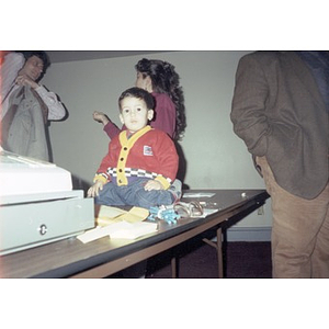 A small child sitting on a desk in front of a cash register.