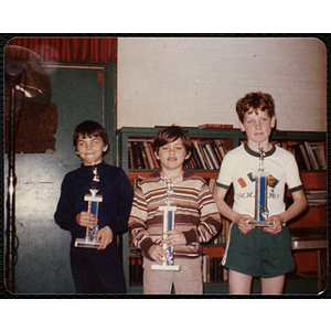 Three boys posing with their Boys' Club basketball tournament trophies