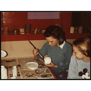 A teenage girl glazing a cup for her art class at the Boys & Girls Club while another looks on