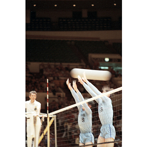 Two male Chinese volleyball players jump to block a ball during a game against the United States team