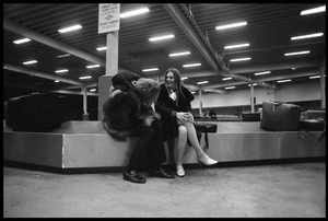 Stephen Stills (in heavy fur coat) and Judy Collins seated on an airport baggage carousel