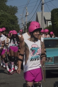 Parade marchers on rollerskates with pink helmets, shorts, and beads : Provincetown Carnival parade