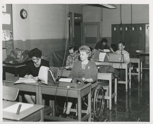 Mrs. Frances Marsala seated in her wheelchair using a typewriter in a room of other students