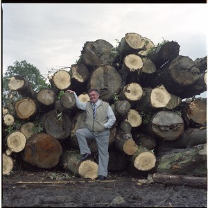 Eddie McIlwaine, journalist with the Belfast Telegraph. His column was named"Ulster Log." Taken beside logs. Includes shot of a helicopter