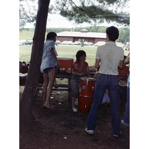 Two woman seated at a picnic table play the drums at a La Alianza staff picnic, while two women and a man stand nearby