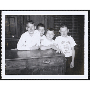 Four Boys' Club members posing behind a table, three of them wearing Boys' Clubs of Boston t-shirts