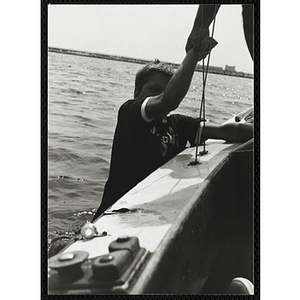 A boy grips the side of a sailboat as man holds him by his wrist in Boston Harbor