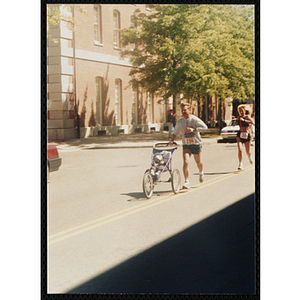 A man pushing a child in a stroller runs the Battle of Bunker Hill Road Race