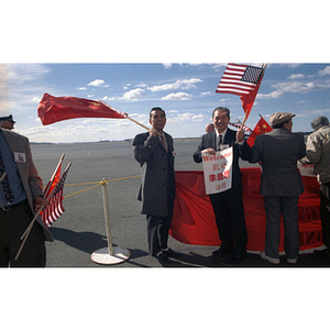 Holding flags and a poster, two male members of the Chinese Progressive Association await the arrival of Premier Zhu Rongji (of China) at Boston Logan Airport