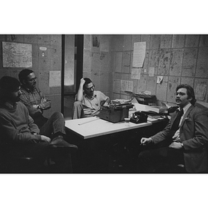 Four men talking around a table in an office, probably connected with the Northeastern News