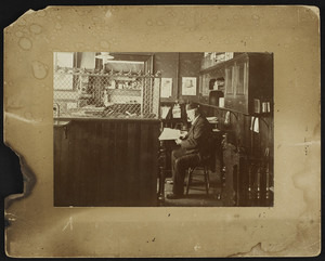 Man sitting in an office, location unknown, 1895