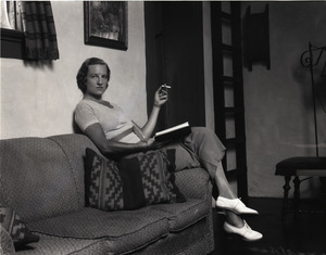 Gertrude Kear (?) posed, seated on a couch, smoking