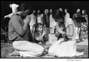 Couple and young girl kneeling, hands in anjali mudra, on stage at the Kohoutek Festival of Consciousness