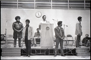 Huey P. Newton speaking at Boston College: Newton at podium with Party members, including David Hilliard (in chair)