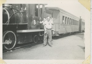 David Kahn with his son Paul on his shoulders posing with a train