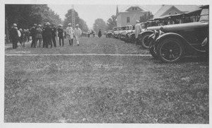 Field with cars parked and people walking and standing