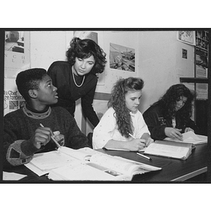 Woman helps children sitting at a desk with textbooks