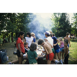 Children surrounding a picnic table at an outdoor barbecue