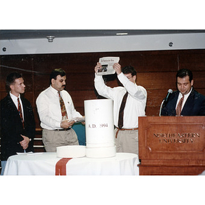 An issue of the student newspaper, the Northeastern News, being placed in a time capsule at the Ell Center dedication