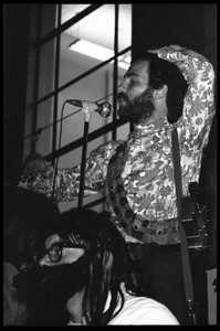 Jerry Rubin, with bandolier and toy assault rifle slung over his shoulder, addressing the audience at the microphone