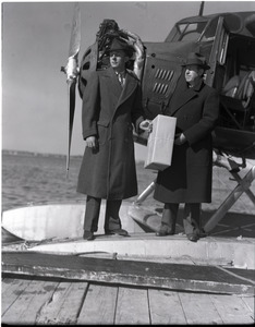 Bill Wincapaw (son) handing a package to William H. Wincapaw (the "Flying Santa Claus") next to their floatplane