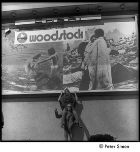 Lacey Mason riding on the shoulders of unidentified man beneath the Woodstock movie billboard, Cheri theater