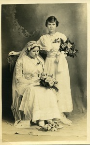 Polish American wedding, bride and bridesmaid: full-length studio portrait with bride seated in chair, head bowed
