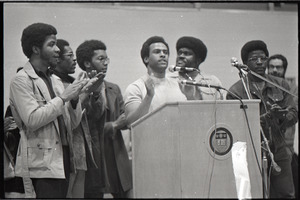 Huey P. Newton speaking at Boston College: Newton at podium with Party members, including David Hilliard (2nd from left) and Elbert Howard (3rd from right)