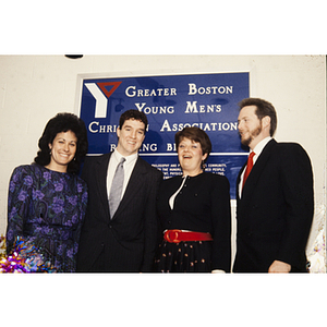 Four adults standing in front of a sign for YMCA of Greater Boston