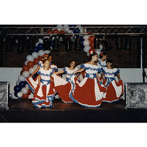 Girls in Puerto Rican flag dresses dance in a circle on stage at the Festival Puertorriqueño