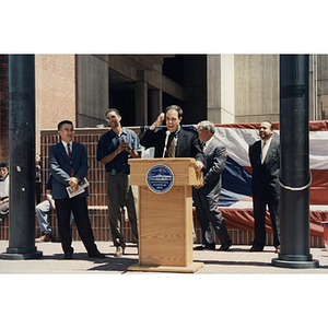 A man makes a face while speaking at a lectern at City Hall Plaza