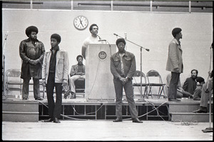 Huey P. Newton speaking at Boston College: Newton at podium with Party members, including David Hilliard (in chair)