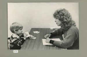 Young boy with cards seated across from woman with notepad