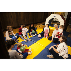 Young children seated with women on gym mats