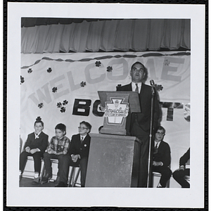 An unidentified man addresses an audience of children at a Boys' Club of Boston St. Patrick's Day inaugural ball and exercises event