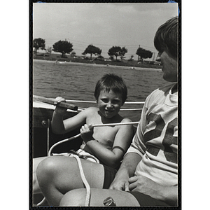 A boy and a teenage boy sit in a sailboat in Boston Harbor