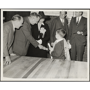 A man shakes hands with a boy who is not visible on the photograph while another man and a woman look on at the dedication and cornerstone laying ceremony for the Charles Hayden Memorial Clubhouse in South Boston