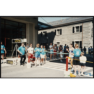 A runner approaches the finish line tape held by two race officials during the Battle of Bunker Hill Road Race