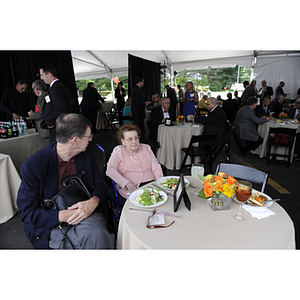 Angelina P. Kostas sits at a table with a man at the reception for the groundbreaking ceremony