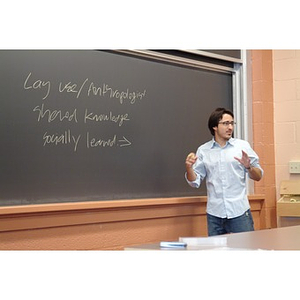 A sociology teacher stands in front of a chalkboard during class