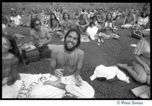 Audience member seated on the lawn, clapping, as he awaits the appearance of Ram Dass at Andrews Amphitheater, University of Hawaii