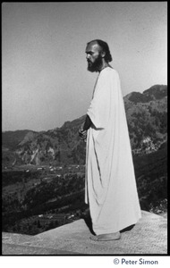 Ram Dass in robes, surveying the landscape from a rock ledge, Lama Foundation