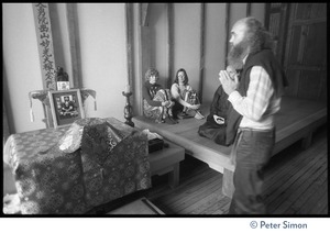 Ram Dass, hands clasped, standing before altar