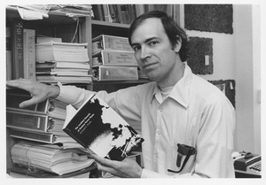 Richard E. Webb seated next to a bookshelf holding his newly published book