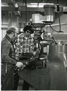 Two unidentified men operating a drill press
